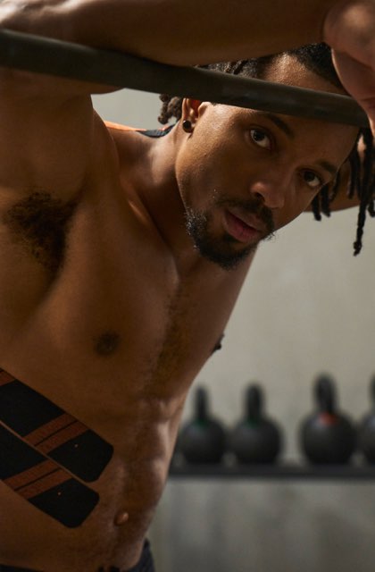 Man leaning against squat rack wearing KT Tape